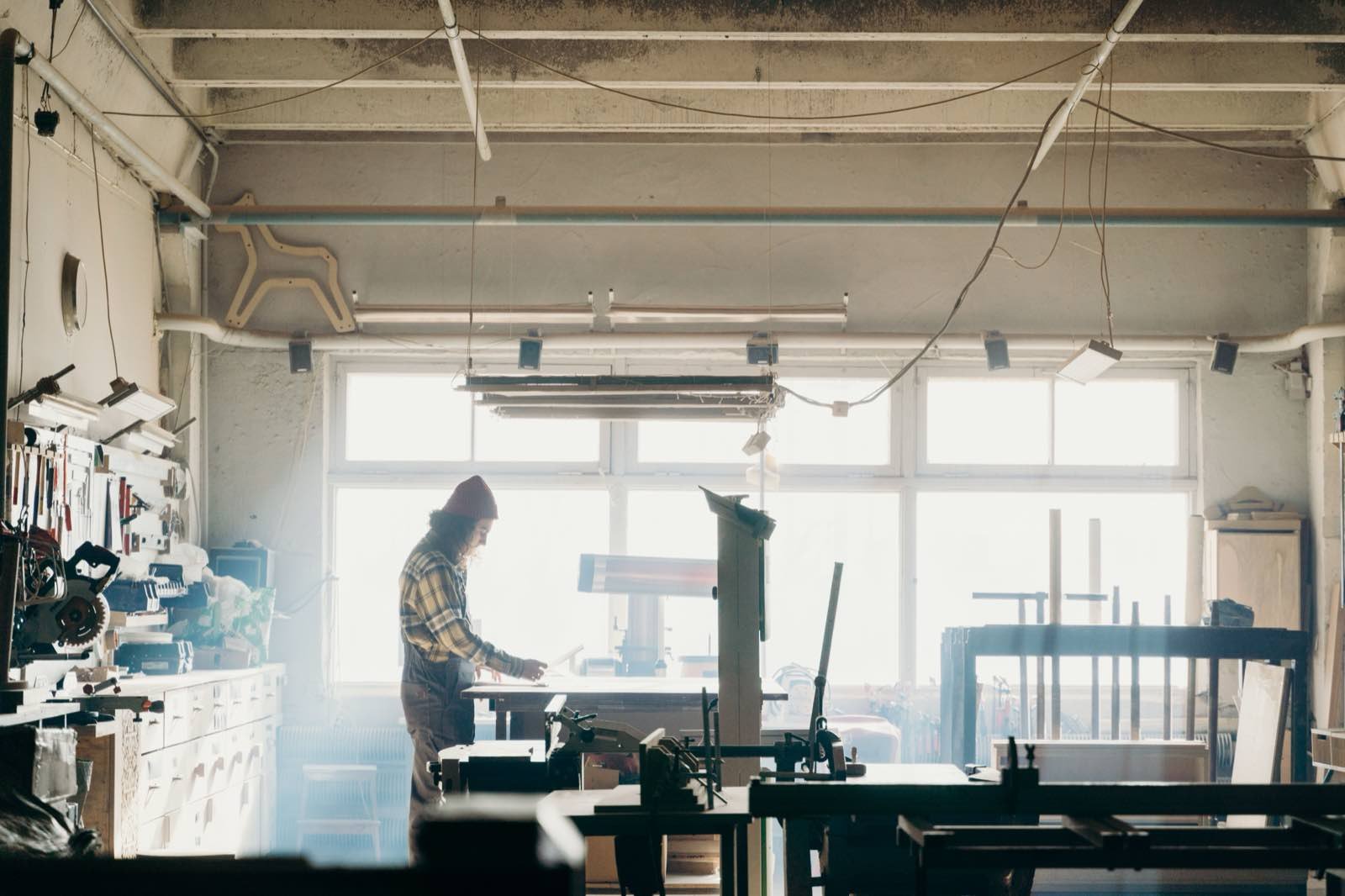 Werkstatthalle im Gegenlicht, eine Person arbeitet an der Hobelbank.